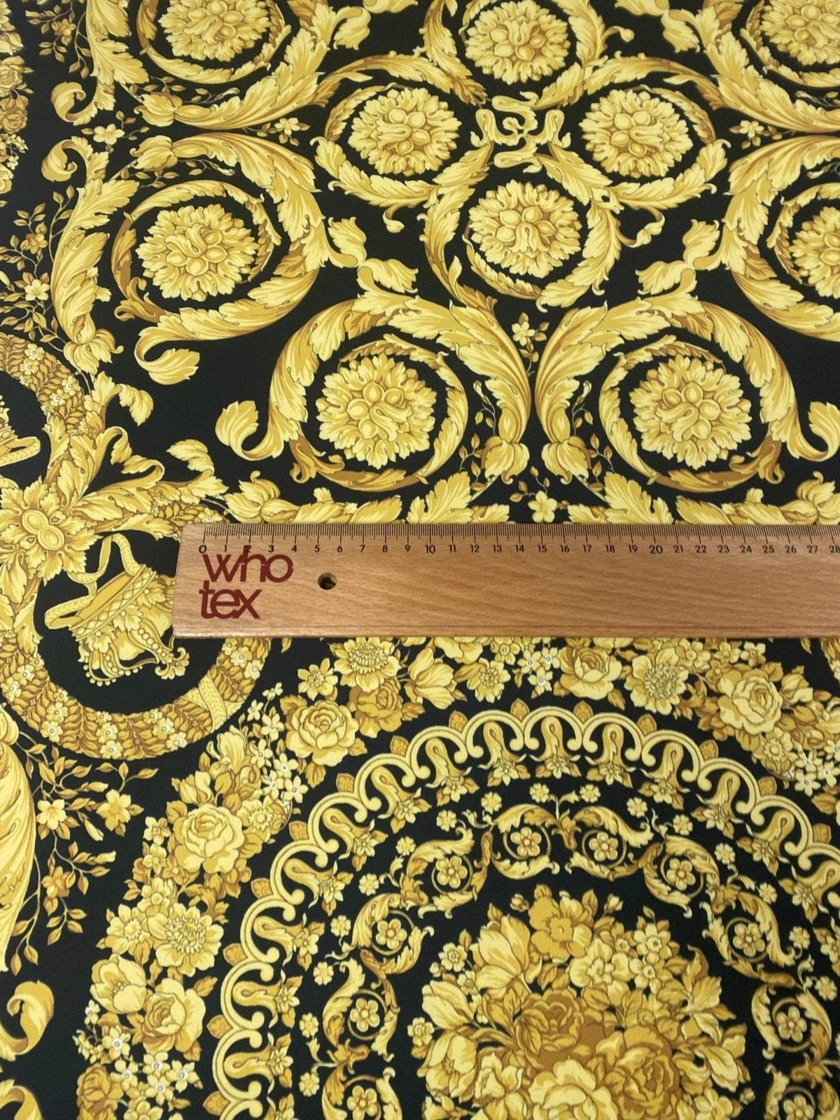 Baroque black and gold upholstery fabric with ornate floral and scroll patterns and a measuring ruler for scale