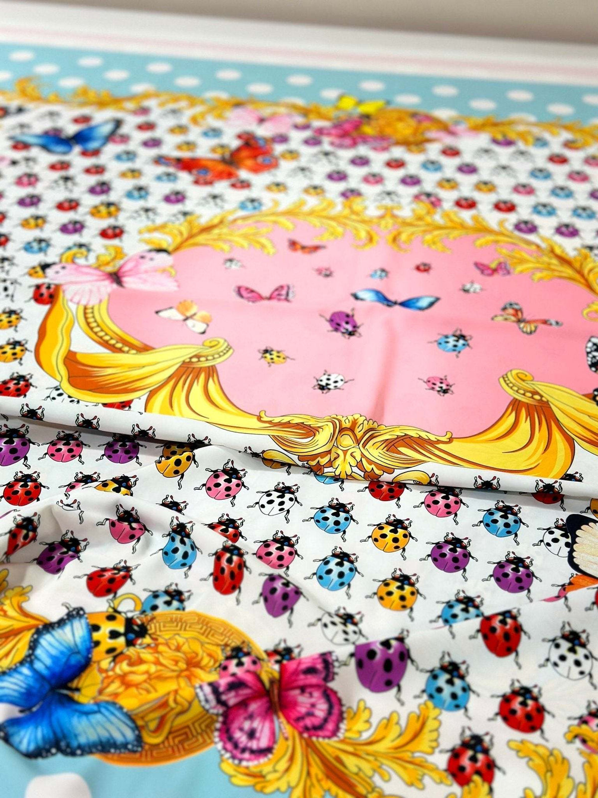 Colorful butterfly and polka dot print fabric with vibrant insects and decorative golden patterns on a white and pastel background