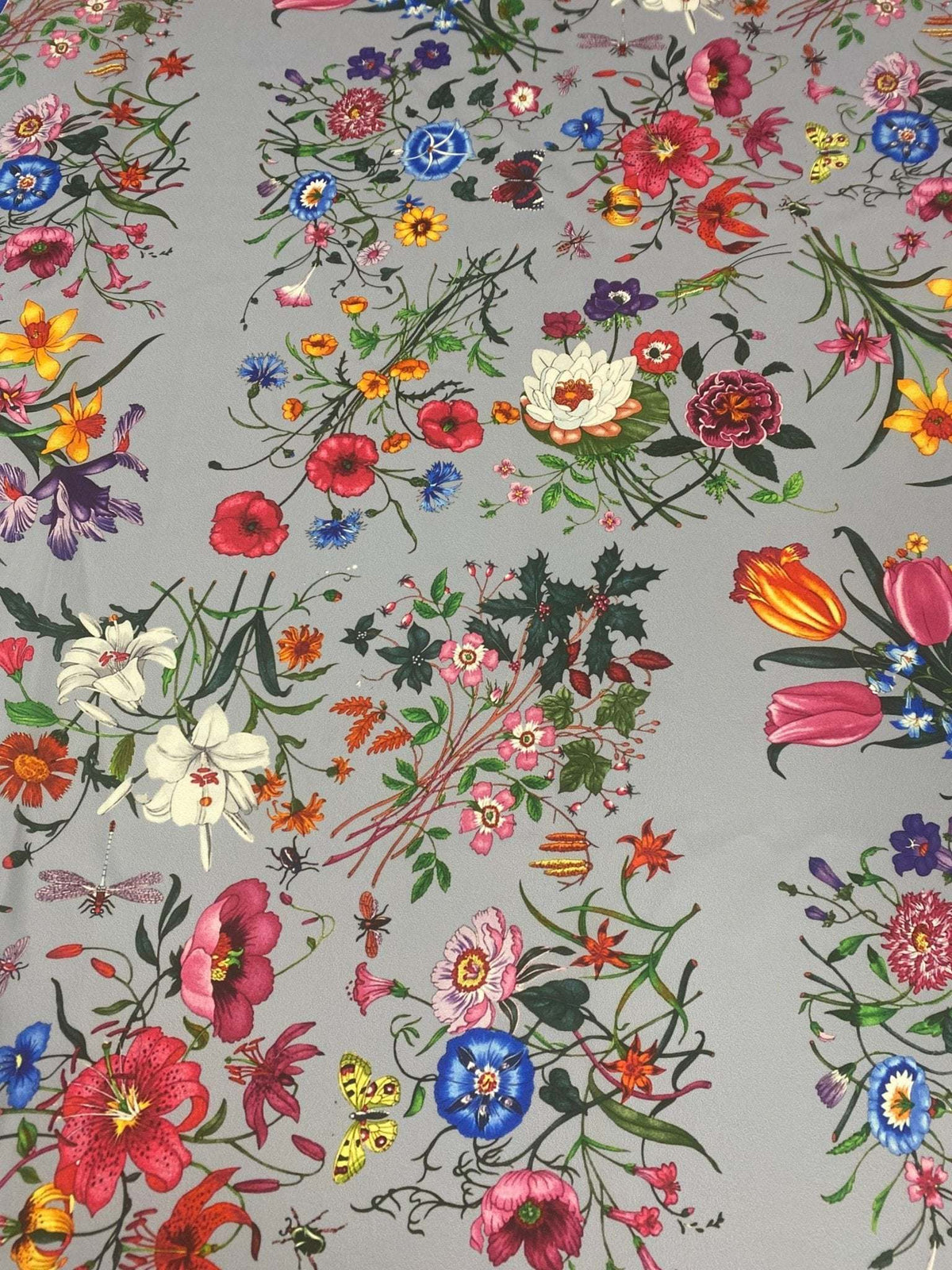 Colorful floral pattern fabric on light grey background with vibrant flowers in various colors and styles