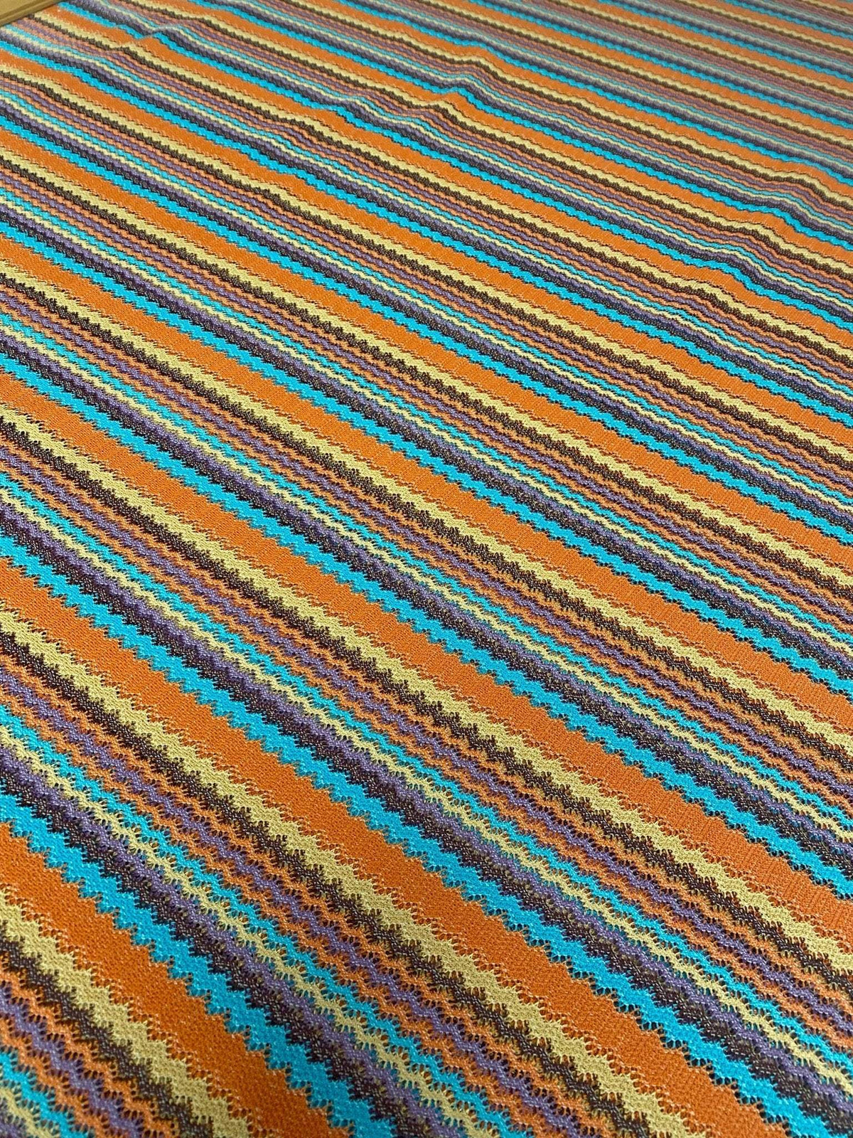 Colorful zigzag stripe knit fabric with vibrant green, orange, blue, and brown tones in a continuous pattern