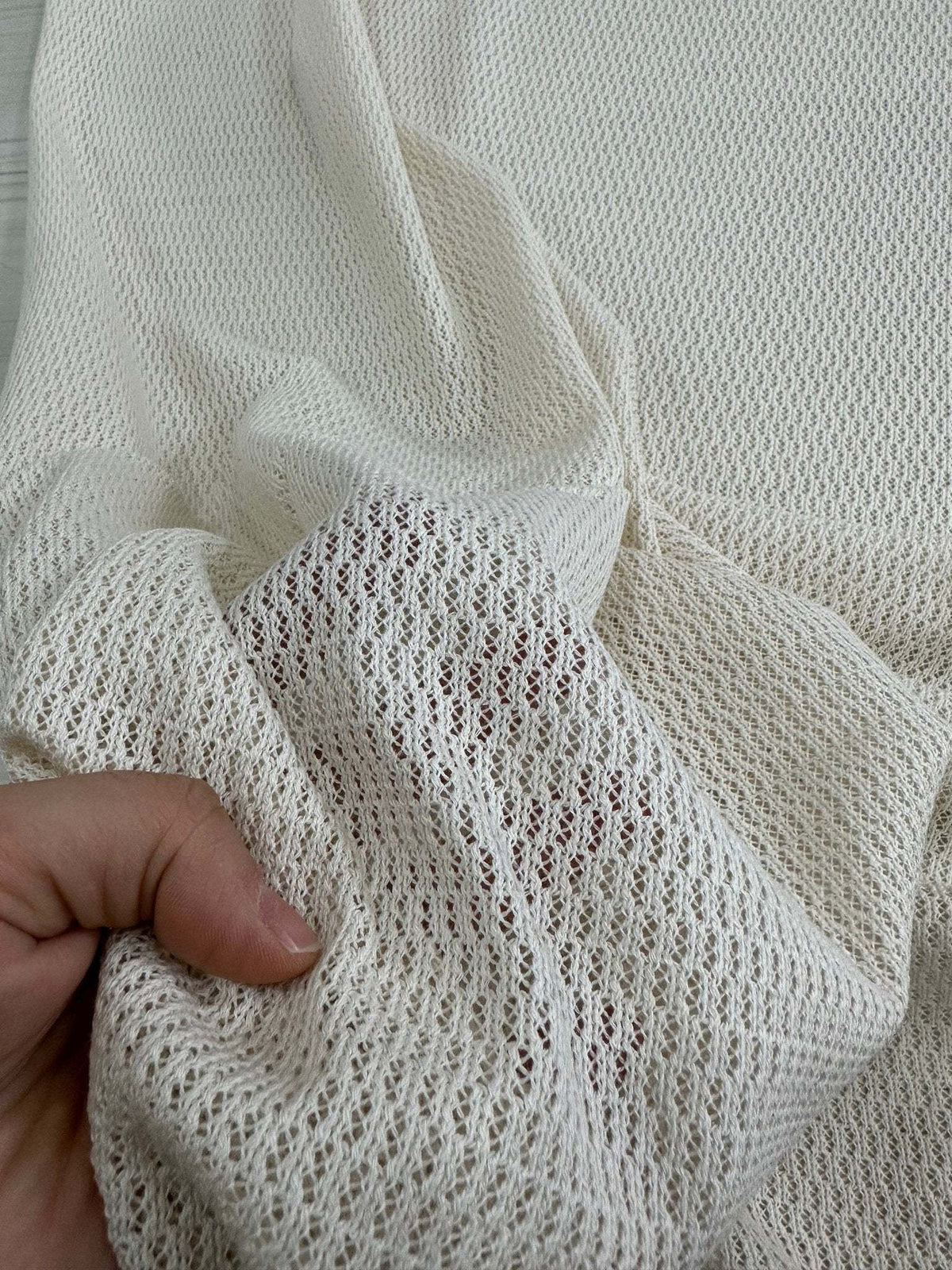 100 cotton off-white fishnet mesh fabric held by hand showing soft open weave texture for crafting and apparel