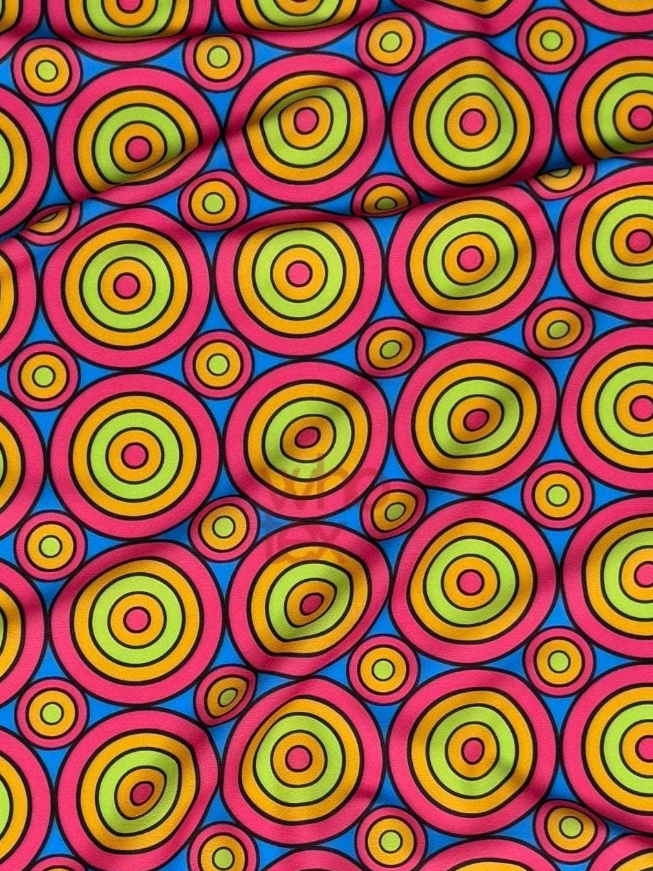 Bright colorful geometric circles print fabric with vibrant concentric ring patterns in yellow, green, blue, and red on a pink background.