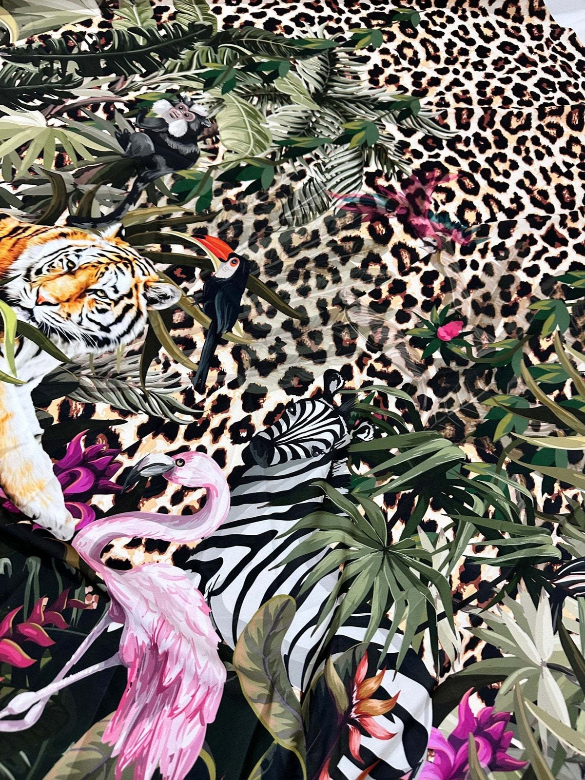 Leopard tropical leaf pattern fabric with tiger, flamingo, zebra, toucan, and lush greenery on a leopard print background