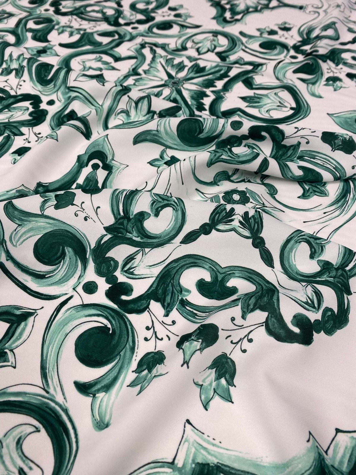Close-up of green and white Majolica pattern fabric with intricate swirls and floral designs on 150cm wide textile