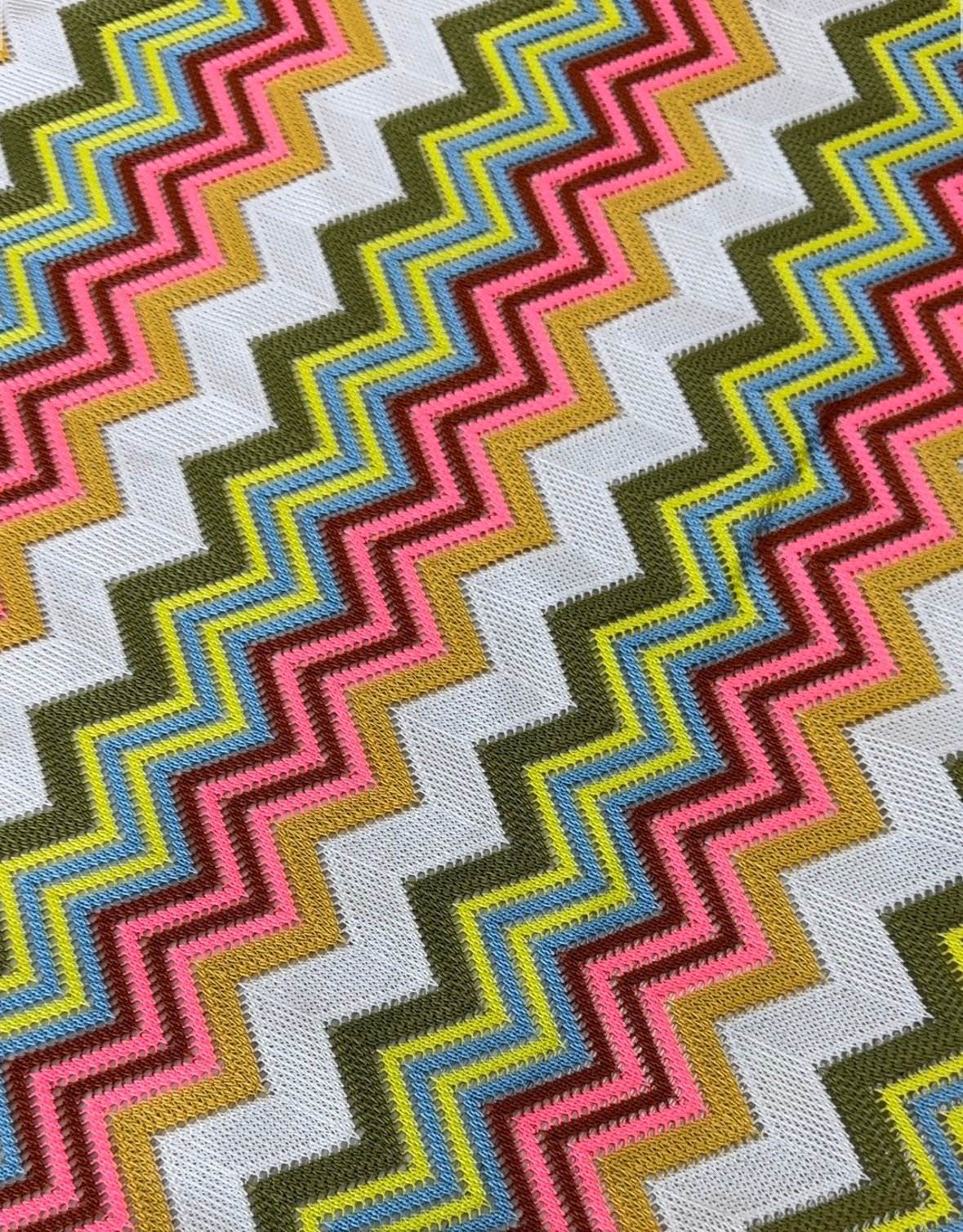 Close-up of multicolor zigzag knit jersey mesh fabric with vibrant pink, blue, yellow, and olive patterns on white background