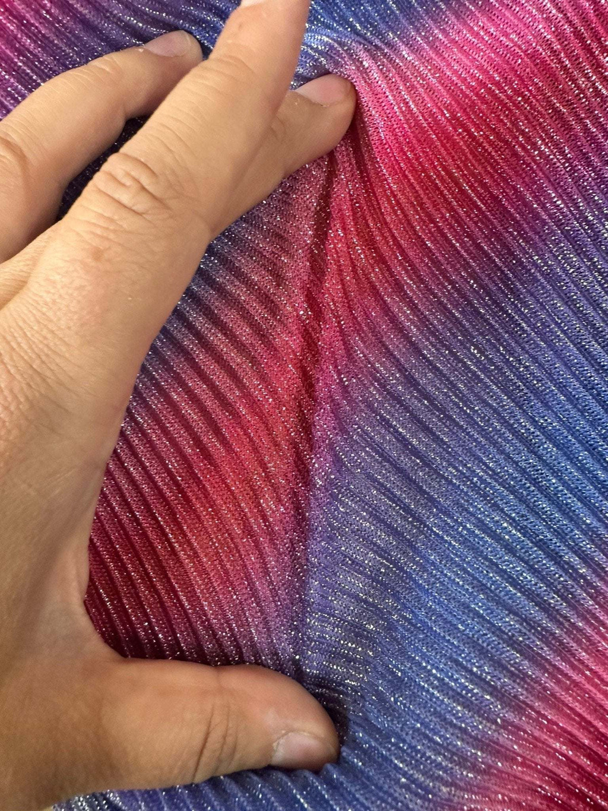 Hand holding shiny pleated power mesh fabric in gradient pink and blue colors with ribbed texture