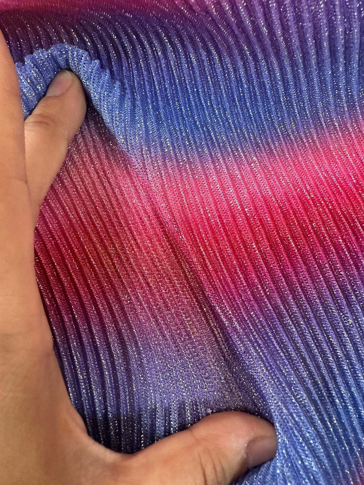 Close-up of pleated power mesh fabric in shimmering gradient shades of purple, blue, and pink held by hand