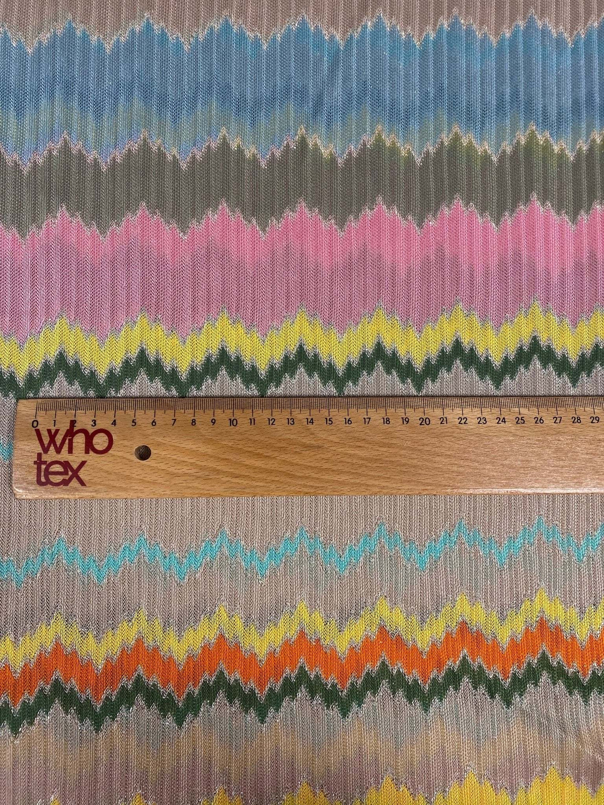Multicolor zigzag mesh fabric knit in green, pink, yellow, and blue tones with ruler for scale