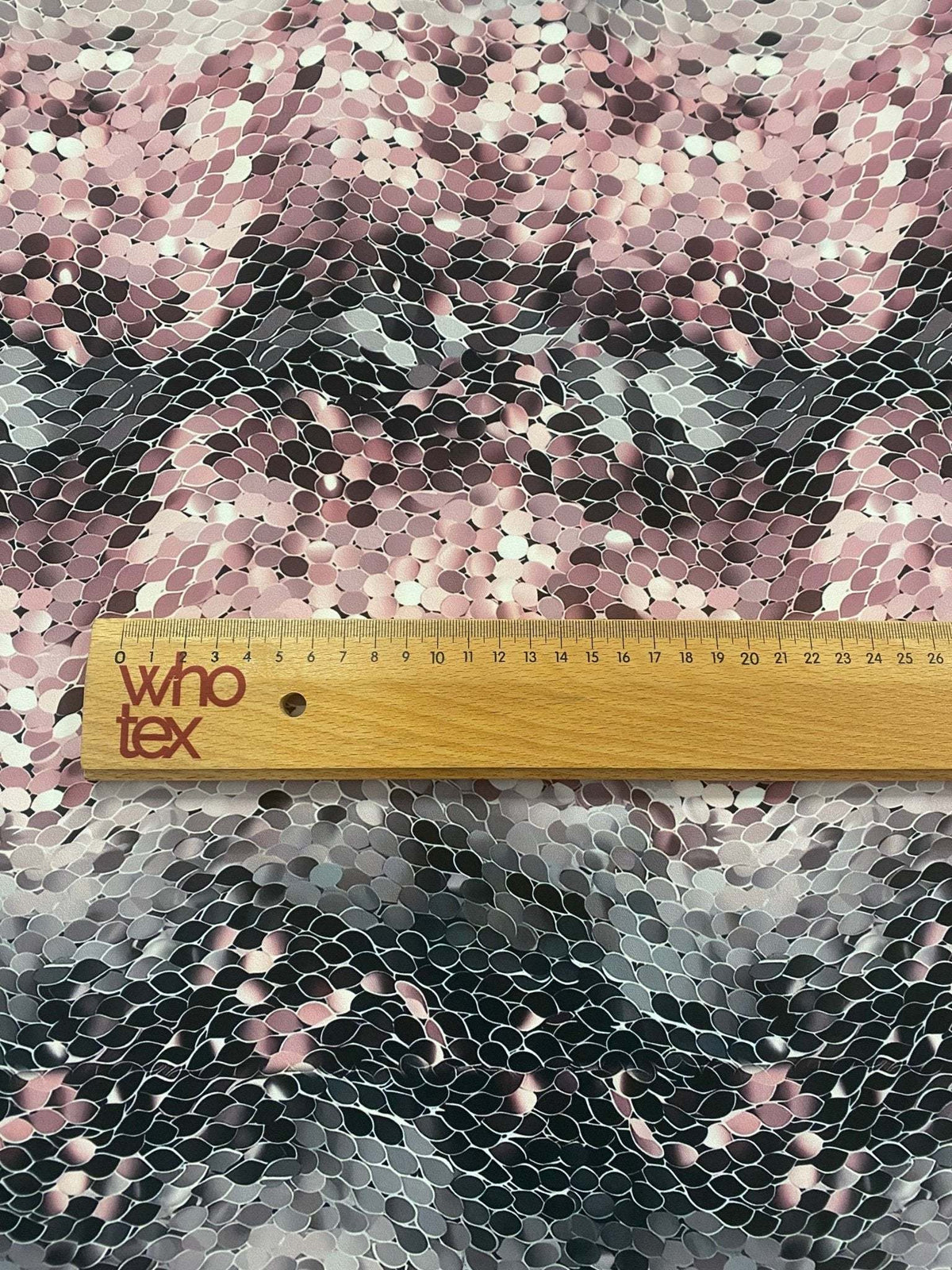 Pink and black abstract scales print fabric with textured optical illusion pattern and a wooden ruler showing scale